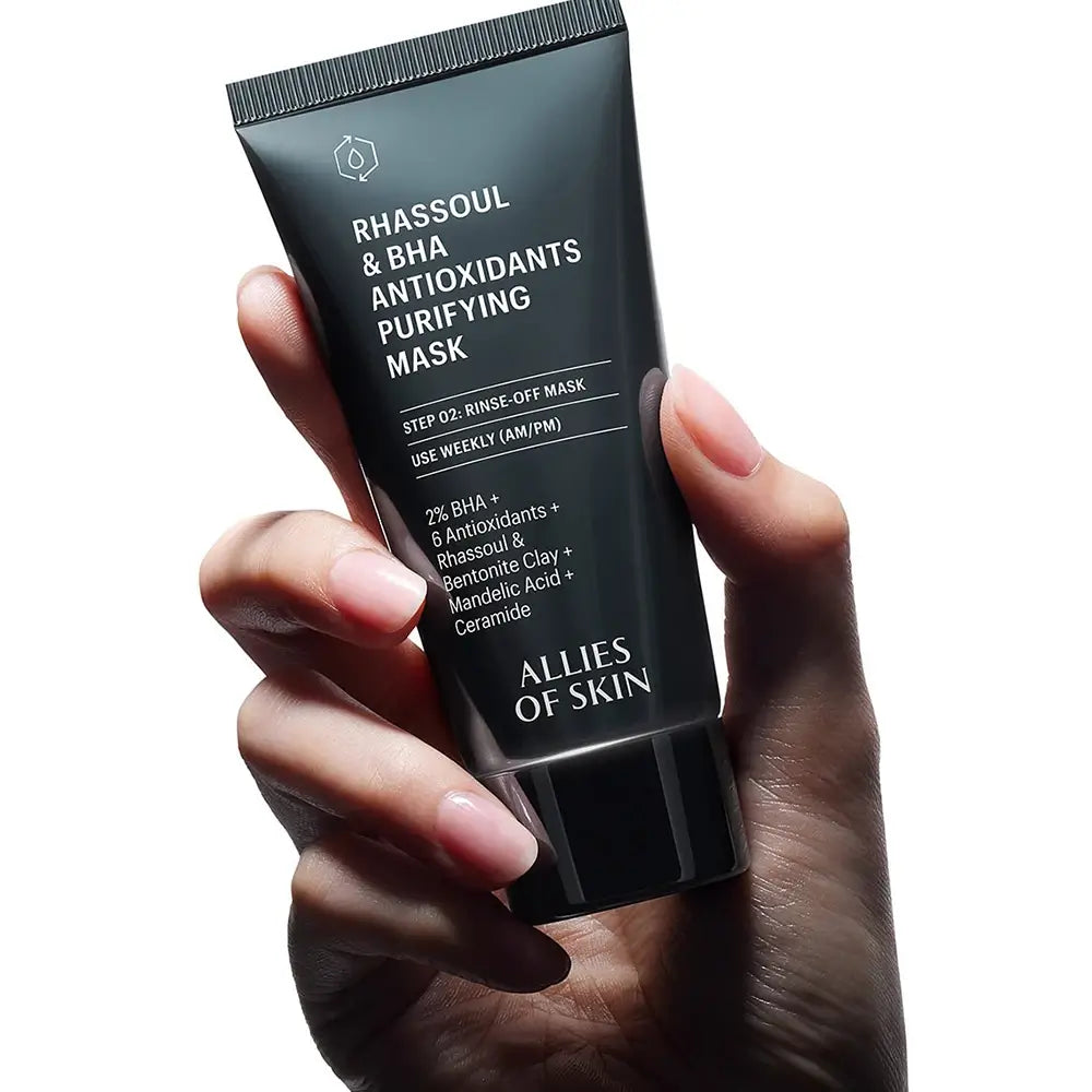 Hand holding a tube of Allies of Skin Rhassoul & BHA Antioxidants Purifying Mask against a white background